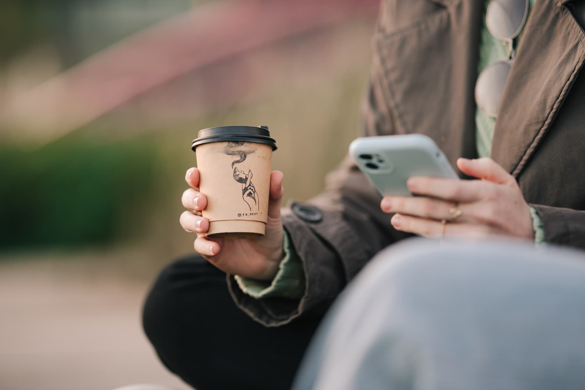 Pessoa sentada ao ar livre segurando um copo do Meio Café, no Parque Una
