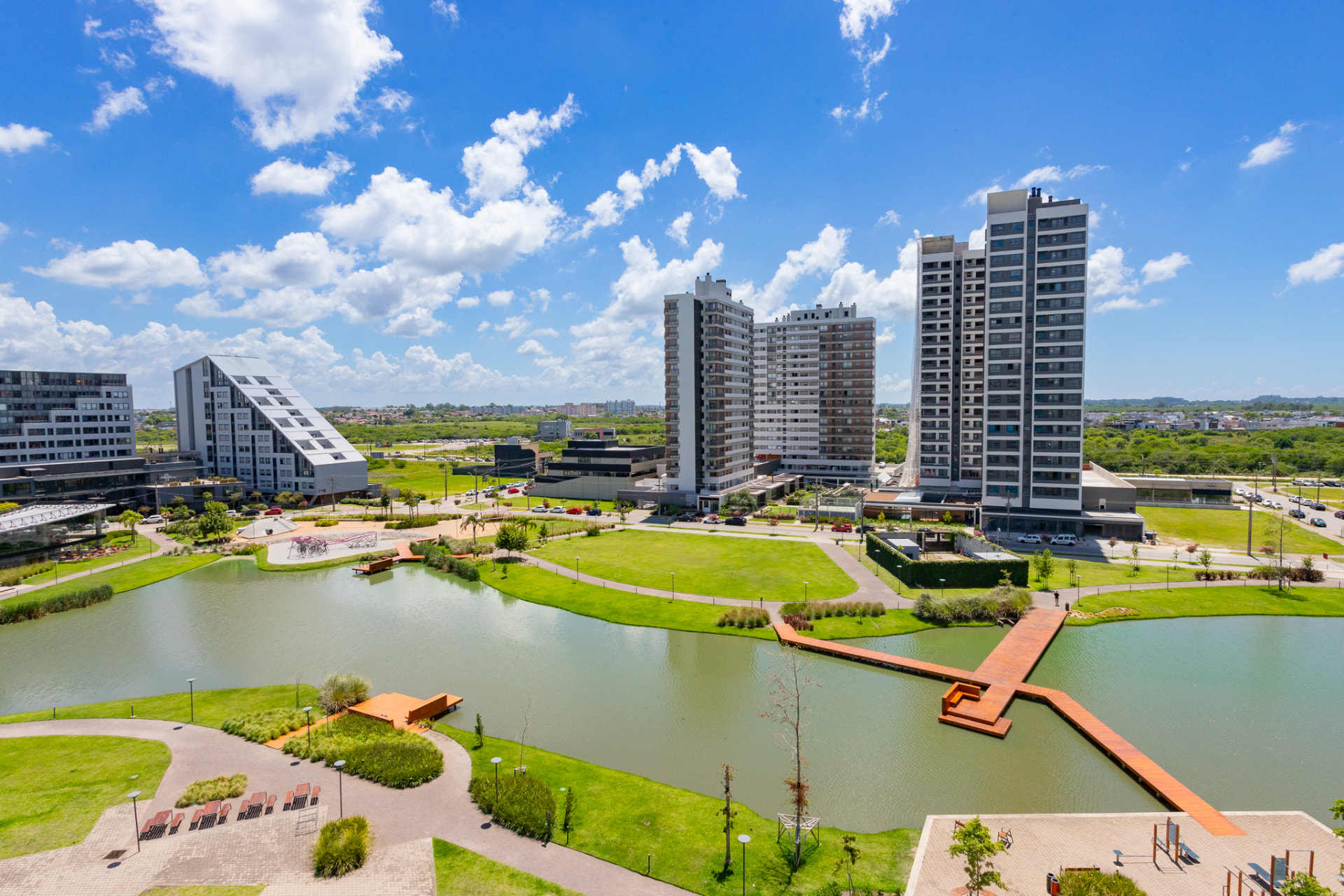 Vista aérea do Parque Una, em Pelotas, com o lago, o deck de madeira e as torres residenciais ao fundo