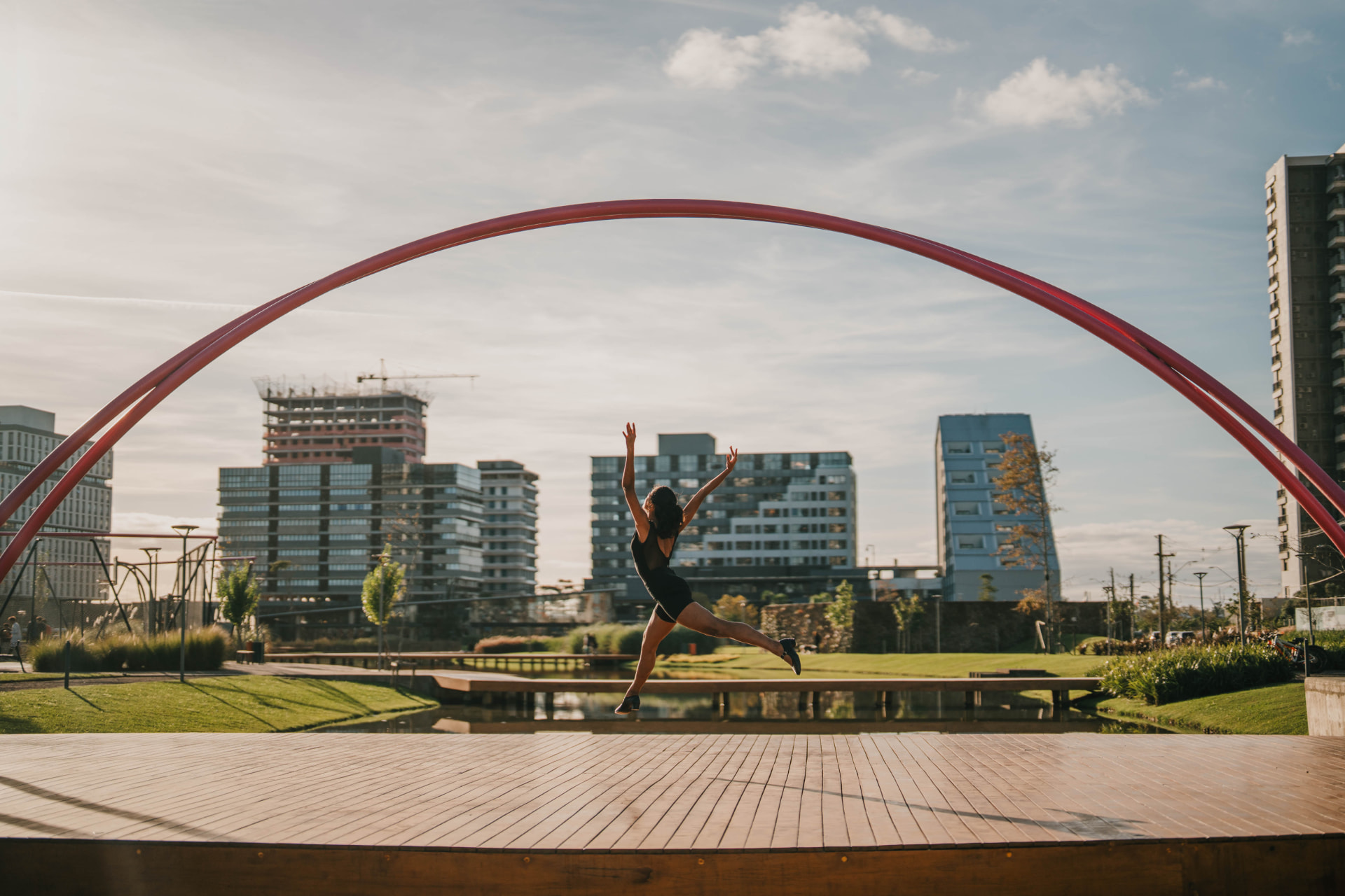 Bailarina saltando no palco de madeira do anfiteatro do Parque Una, sob o arco vermelho