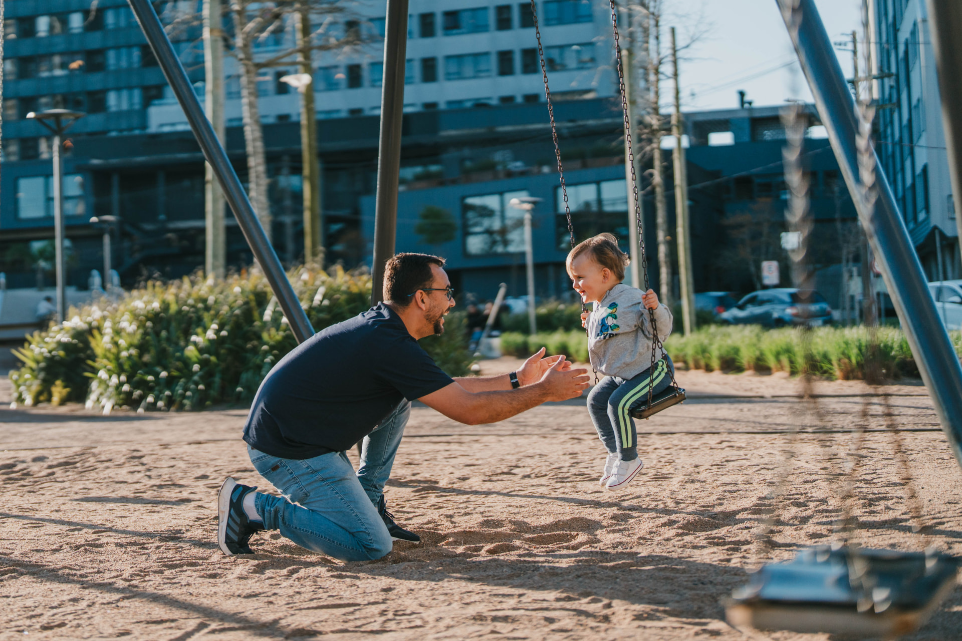 Pai brincando com criança no balanço do playground do Parque Una