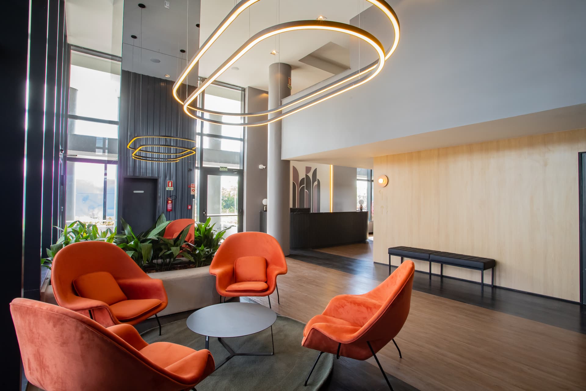 Lobby do Aurora, no Parque Una, com poltronas laranja e luminária circular