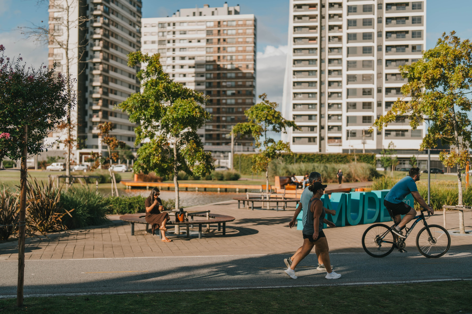 Pessoas caminhando e pedalando na ciclofaixa do Parque Una, com as torres residenciais ao fundo